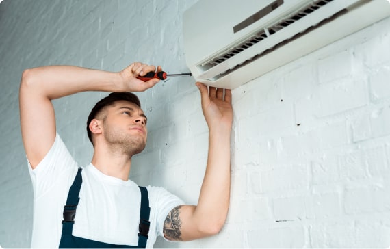 Un hombre arreglando un aire acondicionado en una pared.